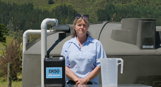 A lady stand next to DX50 Water Tank Treatment with a jug in front of a plastic water tank  